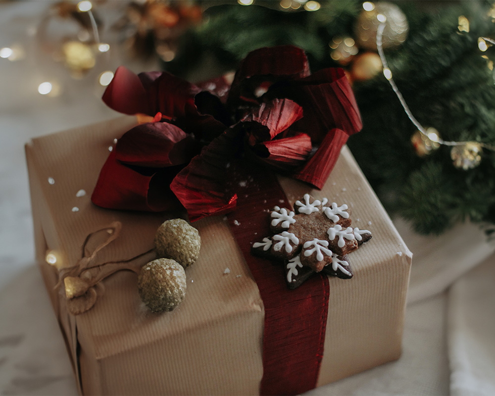 Vianočný darček zabalený v papieri, previazaný mašľou a ozdobený koláčikom.
