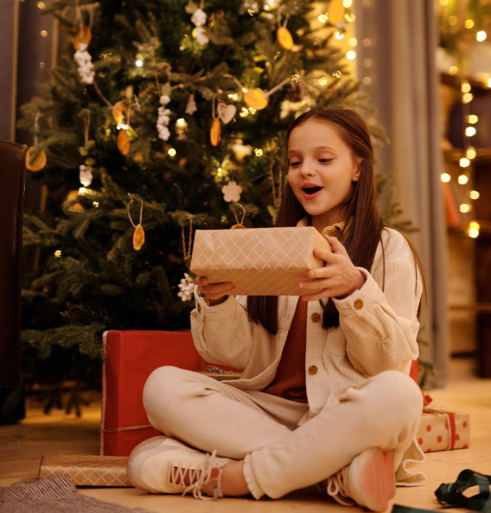 Dievča sa teší z darčeka pod vianočným stromčekom.