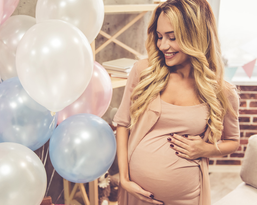 Tehotná žena s úsmevom pozerá na farebné balóny na oslave baby shower