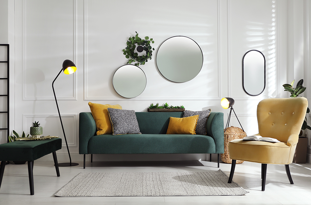 Moderná obývačka vo svetlých farbách so zelenou pohovkou, žltými vankúšmi a okrúhlymi zrkadlami na stene.