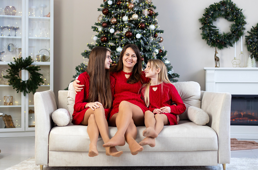 Mama a jej dcéry v červených šatách trávia sviatočný čas spolu pri vianočnom stromčeku.